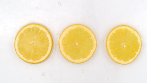 Top-view:-on-a-white-background-a-three-fresh-orange-is-lying-in-the-water-water-drops-are-falling-from-above-and-splashes-are-falling-in-slow-motion-in-all-directions.